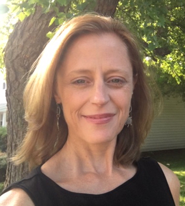 Portrait of a woman outdoors, smiling, with shoulder-length light brown hair, wearing a black sleeveless top and dangling earrings.