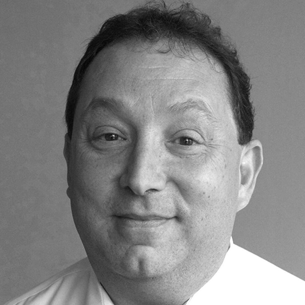 Close-up black-and-white portrait of a smiling middle-aged man looking at the camera with short dark hair.