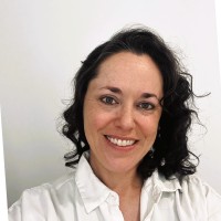 Smiling woman with shoulder-length dark hair wearing a white blouse, posing for a portrait photograph.