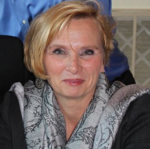 Smiling blonde woman wearing a gray patterned scarf and silver earrings, facing the camera.