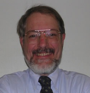 Smiling man with gray beard and glasses in a light blue shirt and patterned tie.