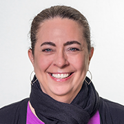 Smiling woman with a dark scarf and hoop earrings, wearing a pink top, facing the camera.