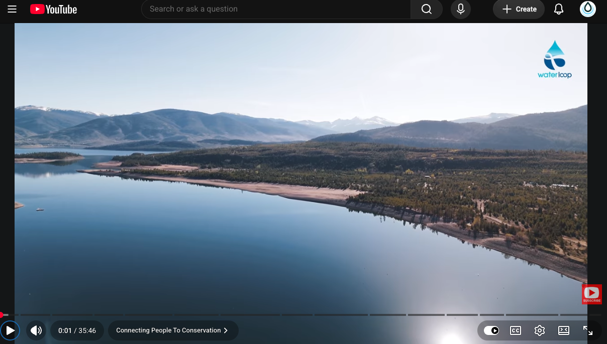Aerial view of a calm lake with a sandy shoreline, forested hills, and distant snow‑capped mountains; WaterLoop logo in the top-right.